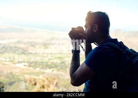 Hier oben ist es ziemlich magisch. Rückansicht eines jungen Mannes, der ein Foto der malerischen Aussicht von der Spitze eines Berges gemacht hat. Stockfoto