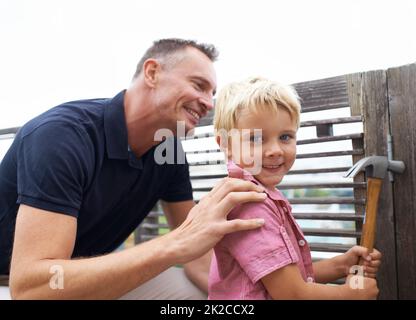 Das Wissen über meine vielen Fähigkeiten weiterzugeben. Ein hübscher Vater lehrt seinen Sohn, wie er einen Hammer benutzt. Stockfoto