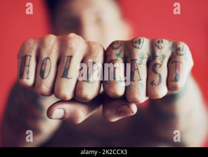 Mit seinem Motto für die Welt zu sehen. Nahaufnahme eines Mannes, der die Tattoos auf seinen Fingern vor einem roten Hintergrund zeigt. Stockfoto