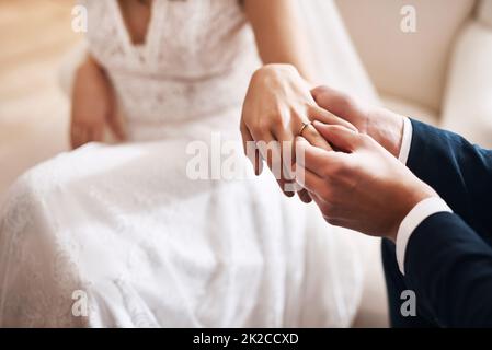 Heres to Forever. Ausgeschnittene Aufnahme eines unkenntlichen Bräutigams, der während der Hochzeit einen Diamantring auf den Finger seiner Frau legt. Stockfoto