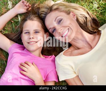 Zeit mit Mama verbringen. Eine glückliche Mutter und ihre junge Tochter liegen draußen auf dem Gras und schauen nach oben. Stockfoto