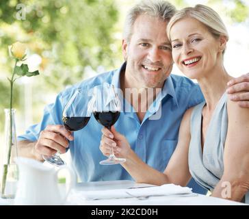 Immer noch verliebt und einander verpflichtet. Glückliches reifes Paar, das seine Liebe mit zwei Gläsern Wein im Freien toaste. Stockfoto
