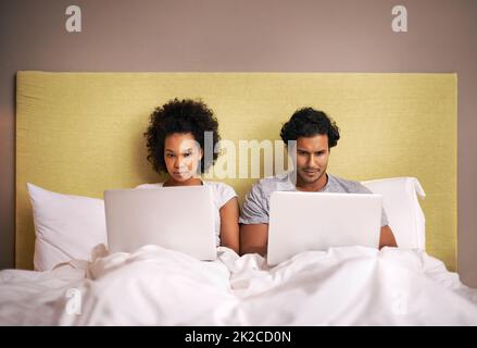 Sitzungssaal im Schlafzimmer. Ein junges Paar im Bett mit ihren Laptops. Stockfoto