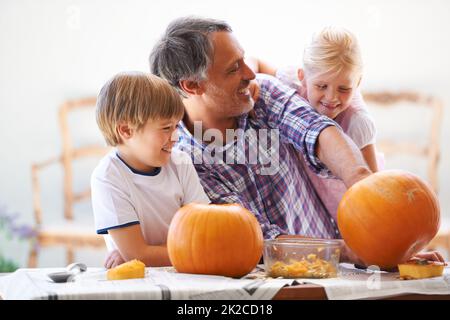 Beim Aushöhlen der Kürbisse abhauen. Ein Vater, sein Sohn und seine Tochter höhlen zu halloween Kürbisse aus. Stockfoto