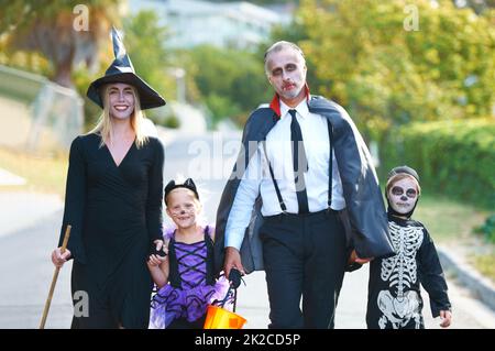 Gemeinsam den Spaß feiern. Eine niedliche Familie, die sich für Halloween verkleidet hat, die ihre Straße entlang läuft. Stockfoto