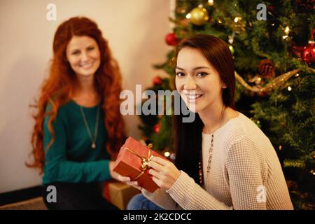 Zeit für Geschenke. Beschnittenes Porträt von zwei jungen Frauen, die an einem weihnachtsbaum sitzen. Stockfoto