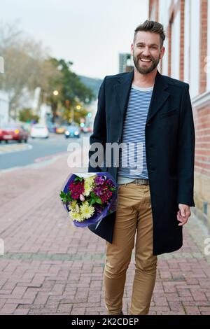 Edelmut ist nicht tot. Porträt eines hübschen jungen Mannes, der mit einem Blumenstrauß in der Hand durch die Stadt läuft. Stockfoto