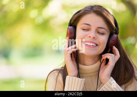 In der Natur und der Musik verloren. Eine attraktive junge Frau, die im Freien Musik hört. Stockfoto