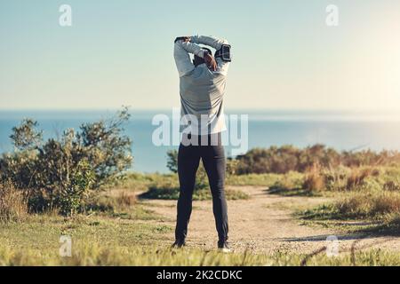 Die Vorbereitung ist der Schlüssel. Rückansicht eines nicht erkennbaren jungen Mannes, der sich vor dem Training im Freien dehnt. Stockfoto