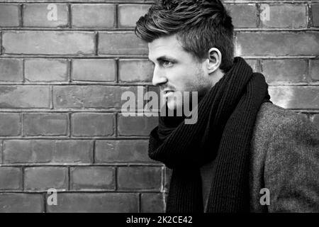 Bringen Sie Stil in den Winter. Schwarz-weiß-Aufnahme eines stilvoll gekleideten jungen Mannes, der auf der Straße steht. Stockfoto