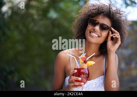 Sieht das cool aus. Porträt einer attraktiven jungen Frau, die eine Sonnenbrille trägt und draußen einen Cocktail genießt.