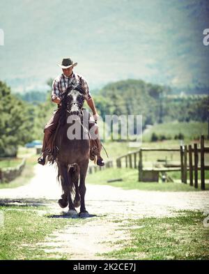 Ja, Aufnahme eines Cowboys, der auf einer Landstraße auf seinem Pferd reitet. Stockfoto