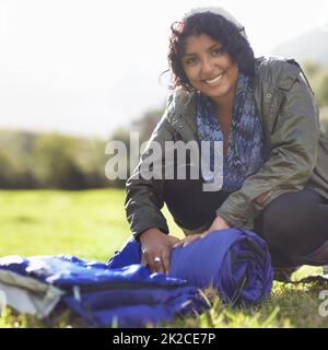 Sie kam bereit zum Lager. Attraktive junge Frau, die einen Schlafsack auf dem Gras ausrollt. Stockfoto