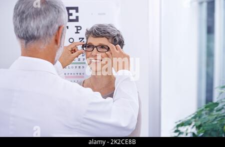 Dieses Paar ist perfekt für Sie. Aufnahme eines Optometriespielers, der eine Brille auf einen Patienten legt. Stockfoto