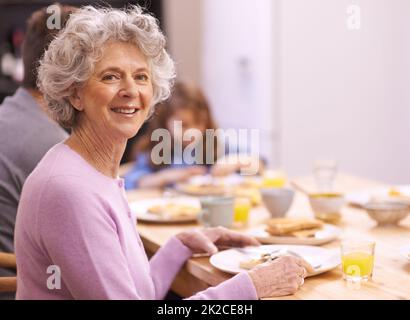 Der beste Start in den Tag. Beschnittenes Porträt einer älteren Frau, die mit ihrer Familie das Frühstück genießt. Stockfoto