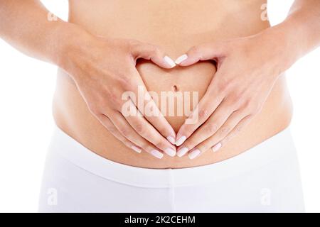 Ihr Kind wird all ihr Herz haben. Eine Schwangerin formt eine Herzform mit ihren Händen über ihrem Bauch. Stockfoto