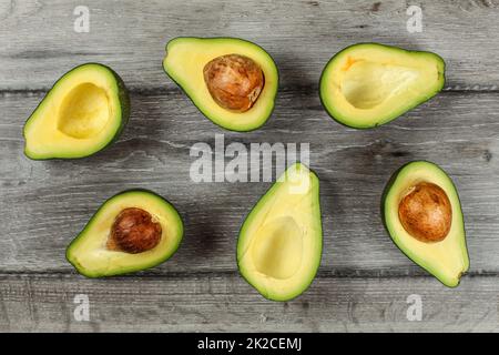 Tischplatte - avocado Hälften, einige von Ihnen mit dem Samen angeordnet, auf grau Holzschreibtisch. Stockfoto