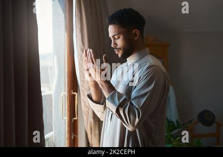 Das Gebet ist die Hingabe aller Ängste. Aufnahme eines jungen muslimischen Mannes, der zu Hause in der Lounge betet. Stockfoto