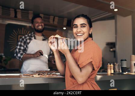 Sie müssen dieses Hotel ausprobieren. Aufnahme einer attraktiven jungen Frau, die in einem Restaurant eine frisch zubereitete Pizza genießt. Stockfoto