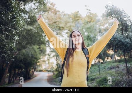 Bestandene Prüfungen. Lächelnde glückliche Schülerin trägt einen gelben Pullover und hebt ihre Arme zum Sieg Stockfoto