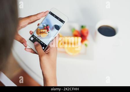 Sieht gut genug aus, um zu essen. Aufnahme einer nicht identifizierbaren Frau, die mit ihrem Smartphone ein Foto von ihrem Frühstück machte. Stockfoto