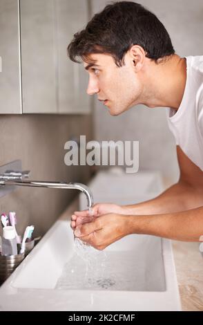 Seine morgendliche Routine aus dem Weg zu bringen. Aufnahme eines Mannes, der in den Spiegel schaute, während er seine Hände unter einen Wasserhahn hielt. Stockfoto