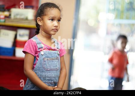 Bildung ist der Schlüssel zu einer besseren Zukunft für sie. Ein kleines, süßes Vorschulmädchen, das sich etwas vor der Kamera ansieht und in ihrem Vorschulraum in Gedanken verloren zu sein scheint. Stockfoto