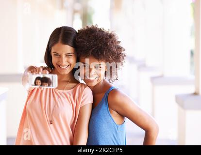 Alle lächeln, wenn Freunde sich aufhalten. Aufnahme von zwei Freundinnen, die ein Selfie auf einem Mobiltelefon machen. Stockfoto