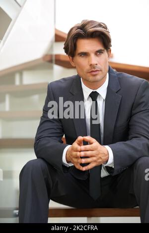 Plant seinen nächsten Geschäftsumzug. Ein hübscher junger Geschäftsmann, der tief in Gedanken auf der Treppe sitzt. Stockfoto