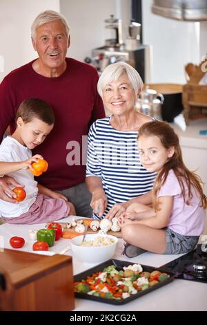 Das Abendessen wird in kürzester Zeit fertig sein. Porträt einer Großeltern, die mit ihren Enkeln eine Mahlzeit zubereiten. Stockfoto