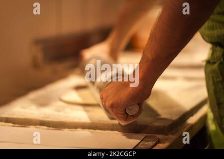 Pizza in der Kreation. Zugeschnittenes Bild einer Person, die Pizzateig ausrollt. Stockfoto