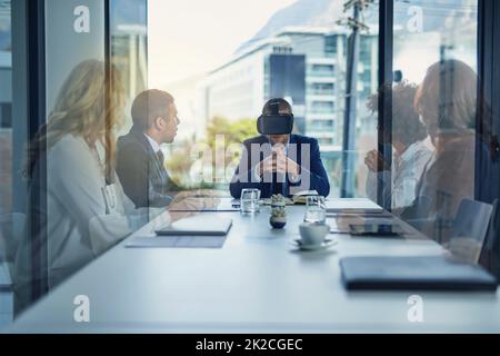 Internationale Barrieren überwinden. Aufnahme eines Geschäftsmanns, der während einer Besprechung im Sitzungssaal ein VR-Headset trägt. Stockfoto