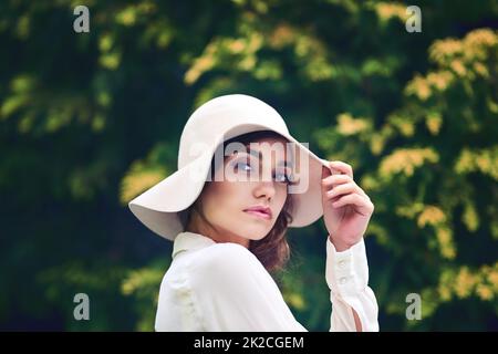 Ihre Schönheit ist absolut einzigartig. Porträt einer attraktiven jungen Frau, die einen stilvollen Hut im Freien trägt. Stockfoto