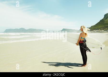 Auf dem Weg ins Meer. Eine junge Surferin, die ihr Surfbrett hält, während sie am Strand steht. Stockfoto