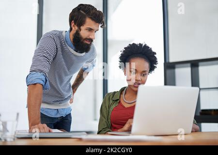 Nur die besten Ideen ins Geschäft bringen. Eine kurze Aufnahme von zwei jungen Kreativen, die in einem Büro zusammen an einem Laptop arbeiten. Stockfoto