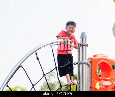 Asiatisches Kind lächelt beim Klettern draußen auf dem Spielplatz Stockfoto