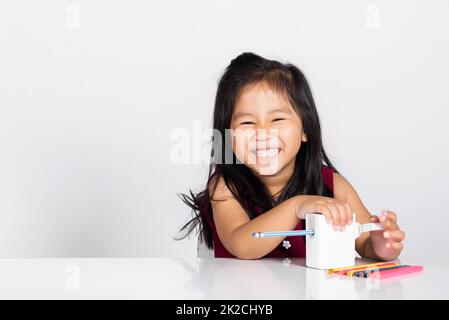 Ein kleines süßes Mädchen im Alter von 3-4 Jahren lächelt mit einem Bleistiftspitzer, während es Hausaufgaben im Studio Einzelaufnahme macht Stockfoto