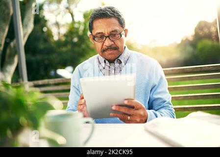 In seinem Ruhestand sozial verbunden bleiben. Aufnahme eines älteren Mannes, der ein digitales Tablet benutzt, während er im Freien frühstückt. Stockfoto