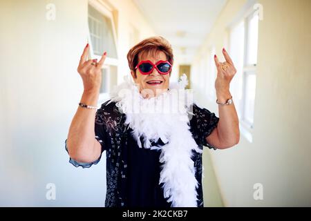 Bereit zum Rocken. Aufnahme einer sorglosen älteren Frau, die eine Brille trägt und Handgesten der Kamera zeigt. Stockfoto