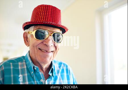 Ich habe diese Brille nicht in einer Weile getragen. Aufnahme eines sorglosen älteren Mannes, der eine Sonnenbrille und einen Hut in einem Gebäude trägt. Stockfoto