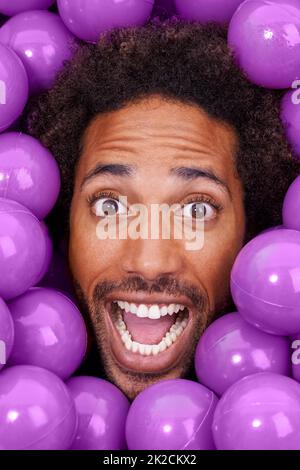 Hey, dieser Ballkasten ist verrückt. Ein junges Gesicht von Schwarzen unter purpurnen Boxenbällen. Stockfoto