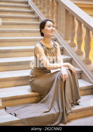 Perfekte Eleganz. Aufnahme einer elegant gekleideten jungen Frau, die auf einer Treppe sitzt. Stockfoto