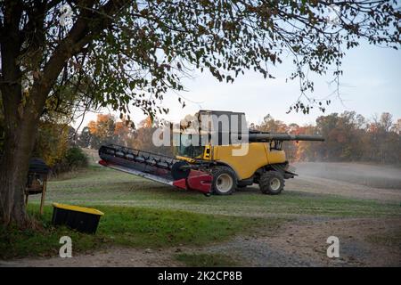 Mähdrescher auf frisch geschnittenem landwirtschaftlichem Feld mit Herbstwald Stockfoto