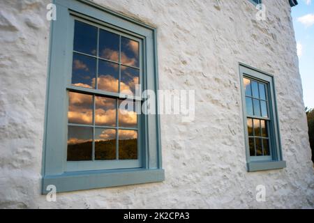 Wolken und blauer Himmel spiegeln sich in den 12-verglasten Fenstern des Kolonialhauses wider Stockfoto