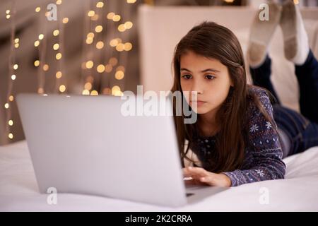 Das Leben eines Tweens. Ein kurzer Schuss eines niedlichen kleinen Mädchens, das ihren Laptop benutzt, während es auf ihrem Bett liegt. Stockfoto