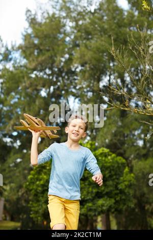 In die Luft. Aufnahme eines Jungen, der mit einem Spielzeug-Flugzeug durch einen Park läuft. Stockfoto