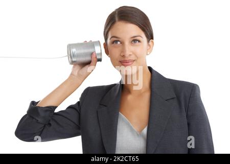 Kommunikation mit der alten Schule. Studioaufnahme einer attraktiven jungen Geschäftsfrau, die ihrem Blechdosen-Telefon zuhört. Stockfoto