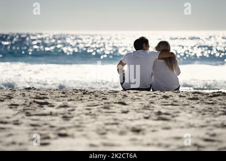 Warten auf den Sonnenuntergang. Ein Paar sitzt am Strand - Rückansicht. Stockfoto