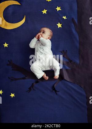 Rock a bye Baby auf der Baumkrone. Konzeptaufnahme eines entzückenden Jungen, der auf einem Baum vor einem imaginären nächtlichen Hintergrund sitzt. Stockfoto