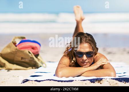 An der Bräune arbeiten. Porträt einer schönen jungen Frau, die am Strand auf einem Handtuch liegt. Stockfoto